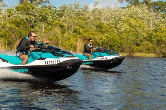 Two people riding jet skis on a lake with trees in the background.