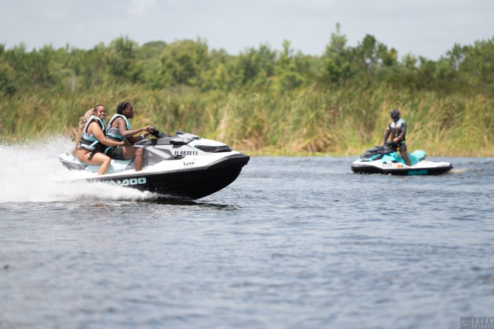 Two people riding a jet ski on a lake, with another person on a jet ski in the background.