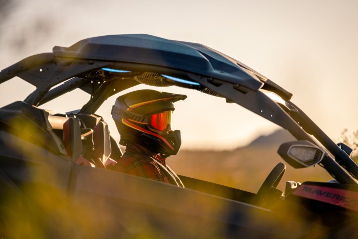 Person in helmet driving off-road vehicle at sunset.