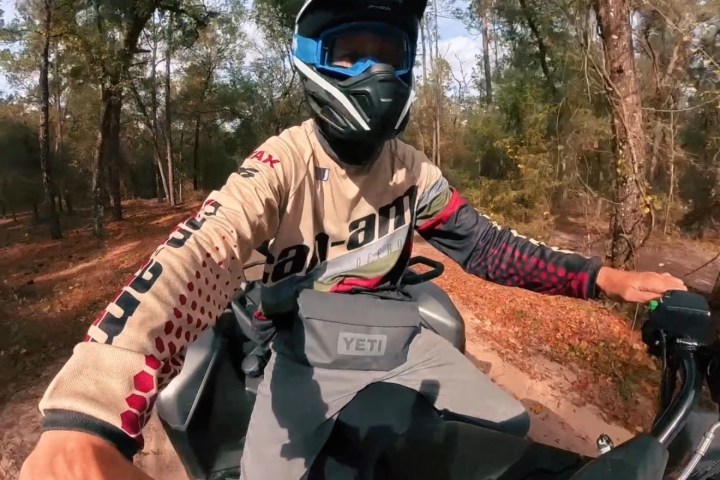 Person wearing helmet riding ATV on dirt trail in forest