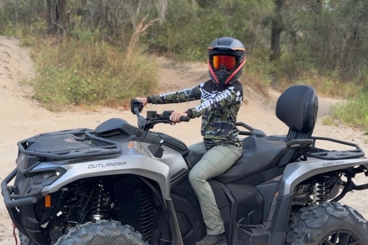 Person on a large ATV in a sandy, wooded area, wearing a helmet.