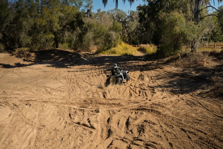 Person riding an ATV on a sandy trail surrounded by trees.
