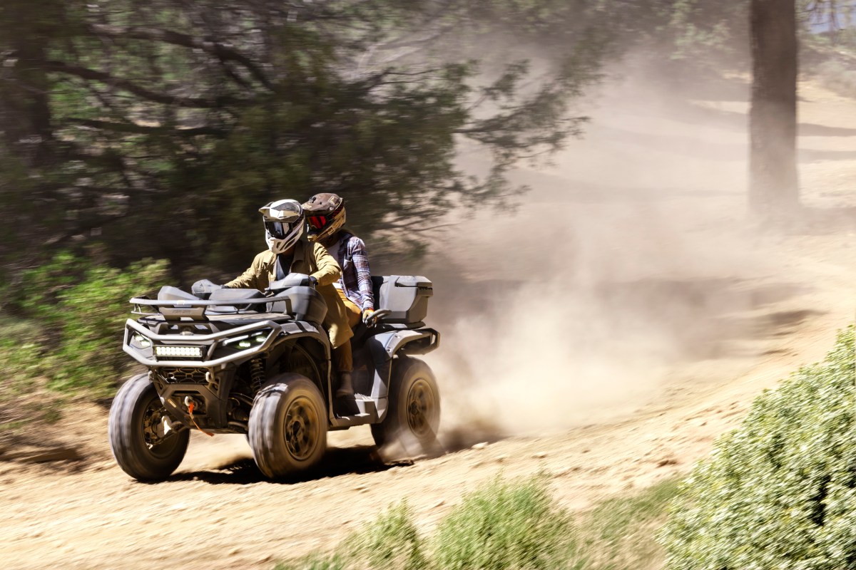 Two people riding an ATV on a dusty forest trail.