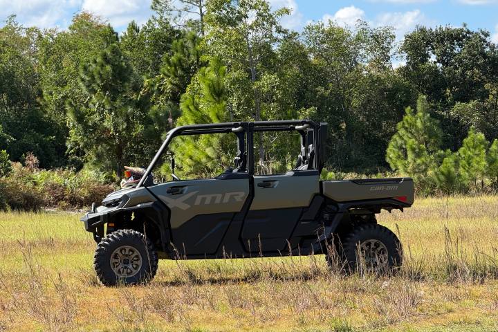 Side view of an off-road vehicle in a grassy field with trees in the background. CAN AM DEFENDER X MR