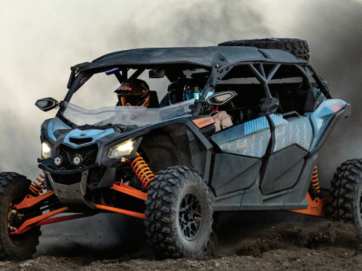 Off-road vehicle kicking up dust on a dirt path, with two occupants wearing helmets.