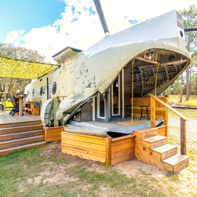 Helicopter converted into a unique outdoor cabin structure with stairs and deck.