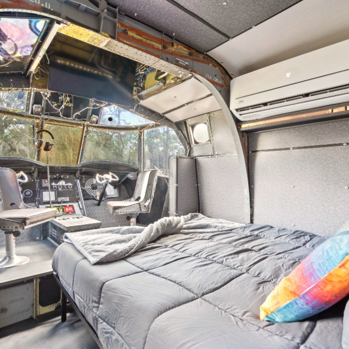 Interior of a converted airplane cockpit with bed and seats.