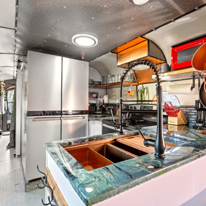 Modern kitchen inside a retrofitted bus with appliances and cookware.