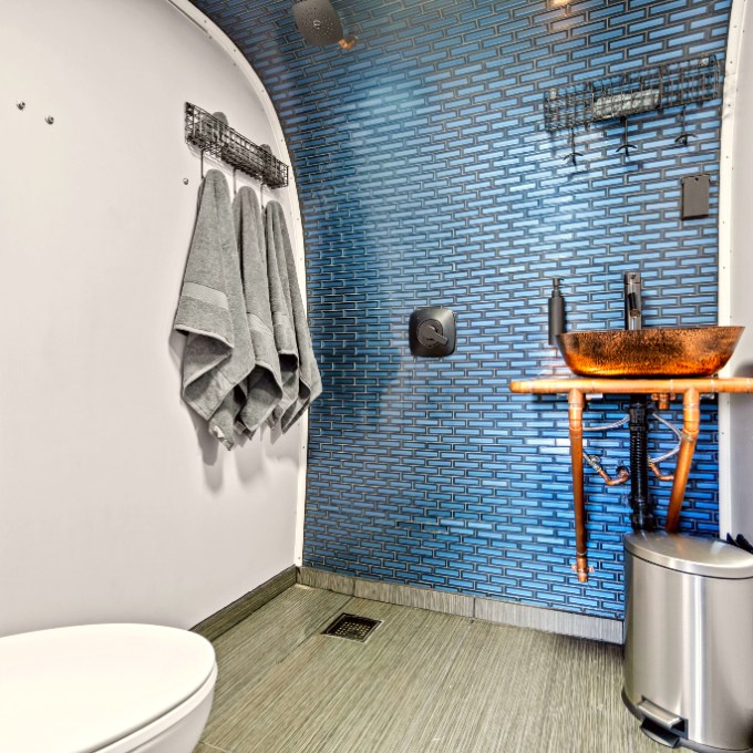 Modern bathroom with blue-tiled wall, round sink, and towels on rack.