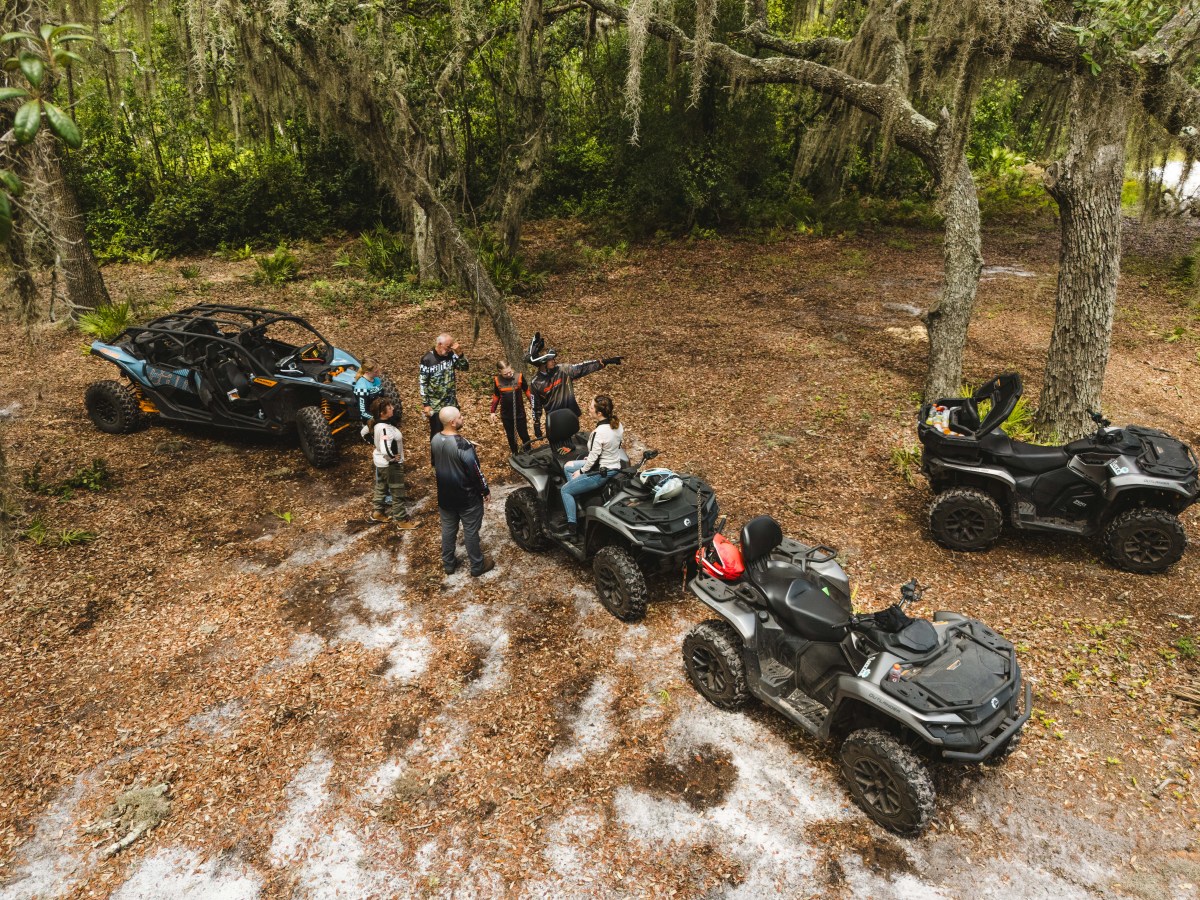 Group with ATVs and a side-by-side vehicle in a wooded area.