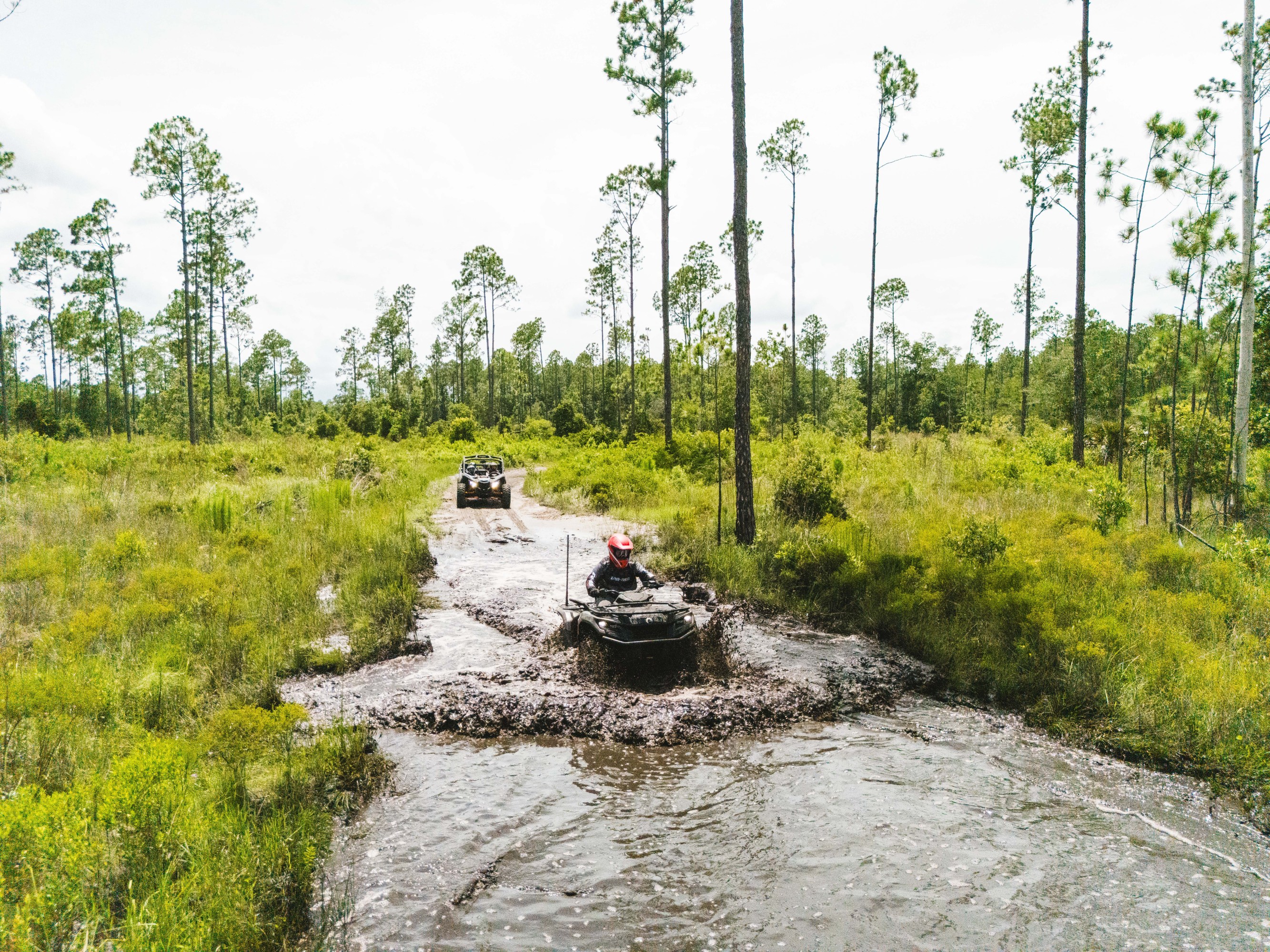 Two all-terrain vehicles driving through a muddy forest trail.