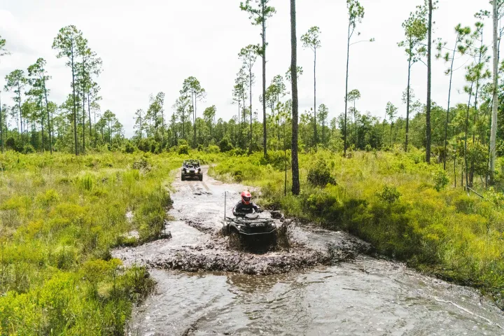 Two all-terrain vehicles driving through a muddy forest trail.